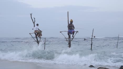Stilt-Fishermen-Sitting-And-Fishing-Using-A-Fishing-Rod-By-The-Ocean-In-Weligama,-Matara,-Sri-Lanka