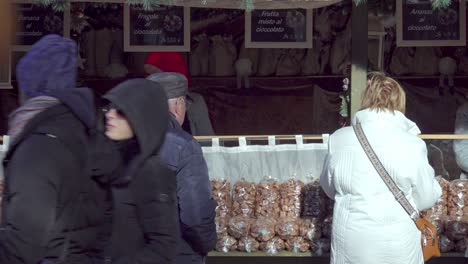 People-stand-in-front-and-walk-past-a-Christmas-stall-at-the-Christmas-market-in-Meran---Merano,-South-tyrol,-Italy