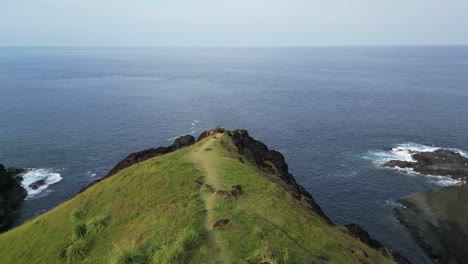 Cinematic-aerial-dolly-of-grassy-cliffside-facing-picturesque-turquoise-ocean-waters-in-Baras,-Catanduanes