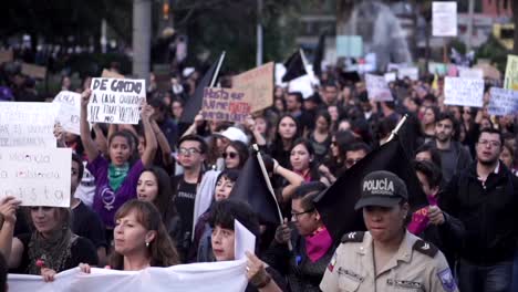 A-crowd-of-women-and-men,-mostly-wearing-black,-are-marching-and-holding-signs-and-black-flags-during-protest-on-the-International-Women's-Day