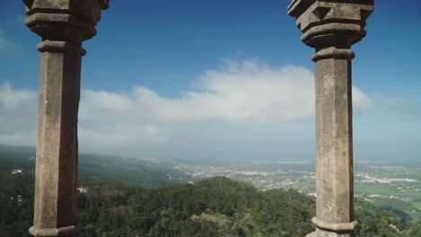 Establishing-shot,-Moving-forward-Between-the-tw-Pillars-on-Pena-National-Palace,-Scenic-view-of-Forest-landscape-and-city-in-the-background