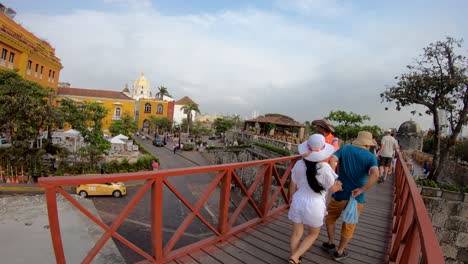 A-couple-of-tourists-are-holding-hands-while-walking-on-a-red-bridge-of-the-old-town-of-Cartagena-de-Indias,-Colombia