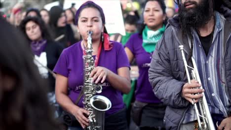 Women-wearing-purple-shirts-are-playing-the-saxophone-and-drums-during-a-protest-and-march-on-the-International-Women’s-Day