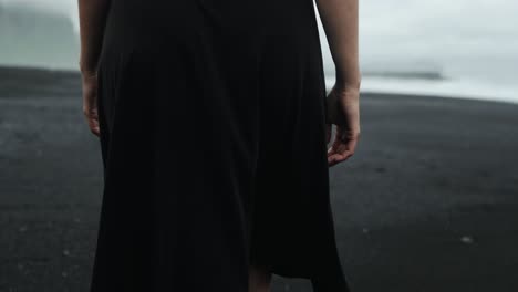 Feet-walking-on-black-sand-beach,-Iceland,-beautiful-redhead-woman-in-black-dress,-slow-motion-tracking,-dramatic-seascape