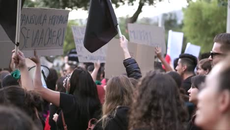 A-crowd-of-men-and-women-are-marching,-chanting-and-protesting-while-holding-signs-and-black-flags-during-the-International-Women's-Day