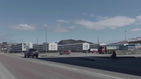 Road-Traffic-Going-Past-With-Of-Artist-Guido-van-Helten-Wall-Art-On-Side-Of-Building-In-Nuuk-In-The-Background
