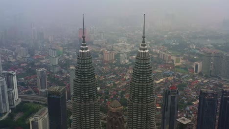Aerial-drone-fly-pedestal-down-along-the-iconic-landmark,-Petronas-KLCC-Twins-towers,-capturing-downtown-cityscape-at-central-district,-Kuala-Lumpur-on-a-foggy-day