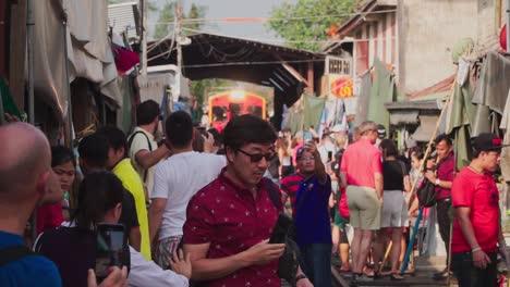 Establishing-Shot,-Tourist-takes-some-picture-and-video-of-the-approaching-train-in-Maeklong-Market-in-Thailand