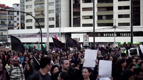 A-crowd-of-women-and-men-wearing-black-clothes-are-holding-signs-and-black-flags-and-a-LGTB-flag-during-a-march-and-protest-on-the-international-Women's-Day