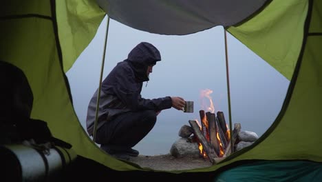 Static-Shot-From-Tent-Of-Camper-Having-His-Warm-Drink-Watching-Bonfire