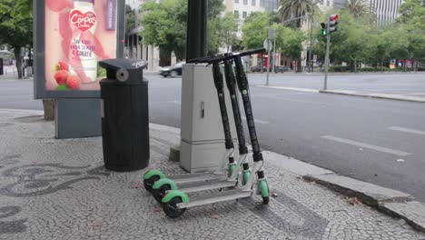 Tres-Scooters-De-Pago-Estacionados-En-La-Acera-Junto-A-La-Carretera