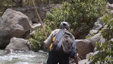 Old-Man-With-Backpack-Stepping-Carefully-On-Rocks-Towards-River-For-Fishing,-Obrajillo