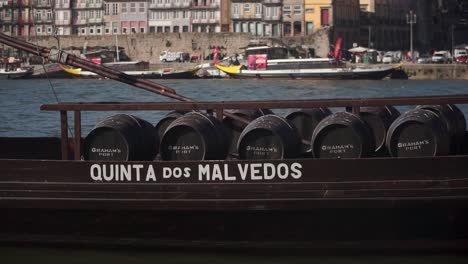 Plano-Medio,-Barco-Tradicional-Con-Barril-Flotando-En-El-Río-Duero-En-Porto,-Casco-Antiguo-Al-Fondo