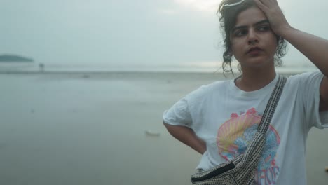 Junge-Indische-Frau-Blickt-Anmutig-In-Die-Kamera,-Während-Sie-An-Einem-Bewölkten-Strandtag-Heranzoomt
