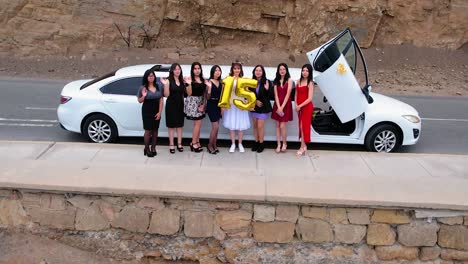 Aerial-video-of-girls-holding-a-15-made-of-ballons-in-front-of-a-white-limousine