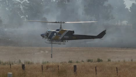 Helicóptero-Flotando-Sobre-La-Presa-Con-Fuego-De-Hierba-En-Segundo-Plano.