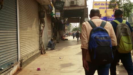 Gente-Caminando-Por-La-Calle-De-Chandni-Chowk-En-La-Vieja-Delhi,-Persianas-Cerradas-De-Las-Tiendas-Locales-Durante-El-Día,-India