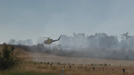 Helicopter-lifting-off-after-picking-up-dam-water,-rotor-blades-spraying-water-off-dam
