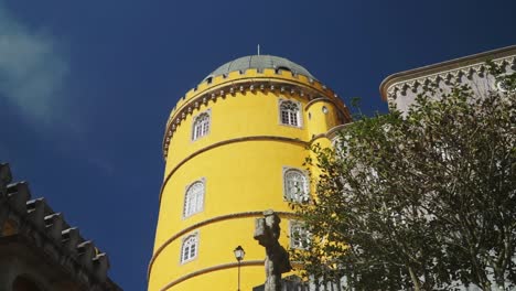 Tiro-En-Movimiento-Hacia-Arriba,-árbol-Verde-Y-Cruz,-Torre-Amarilla-Del-Palacio-Nacional-De-Pena-En-Portugal,-Cielo-Azul-En-El-Fondo