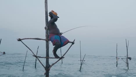 Hombre-De-Sri-Lanka-Sentado-Sobre-Pilotes-De-Madera-Y-Pescando-En-La-Costa-De-Weligama,-Matara,-Sri-Lanka