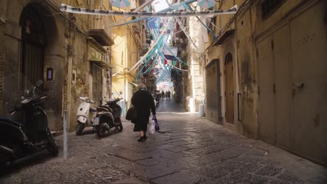 Flags,-bunting-and-streamers-stretched-across-the-street-of-Naples,-Old-woman-walking-through-the-narrow-lanes