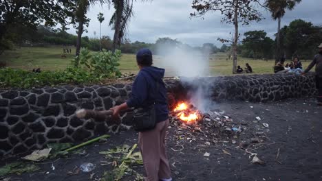 Balinese-Women-Burns-Plastic-Trash-Making-Fire-at-the-Beach,-Pollution-and-Smoke-Environmental-Issues-in-Bali,-Indonesia,-Saba-Beach-Gianyar