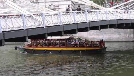 Un-Barco-Que-Transporta-Turistas-Pasando-Por-Debajo-Del-Puente-Cavenagh-Sobre-El-Río-Singapur.