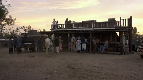 Wild-west-reenactment-scene-in-front-of-saloon-wooden-building-with-people-passing-in-period-costume