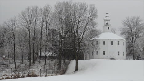 Slow-motion-panning-shot-of-wet-snow-falling-in-early-spring-at-The-Old-Round-Church-in-Richmond,-Vermont