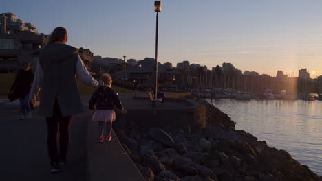 TRACKING-SHOT-of-a-Mother-and-Daughter-Walking-Along-the-Seawall-During-Sunset