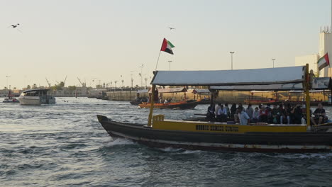 Ferry-Abra-Saliendo-Y-Llegando-Al-Puerto-De-Dubai-Creek-Durante-La-Puesta-De-Sol-En-Dubai,-Emiratos-árabes-Unidos