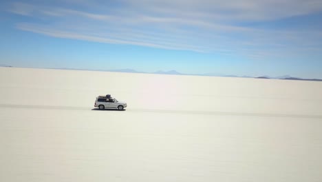 Aerial-tracking-drone-shot-following-a-car-driving-on-white-salt-desert,-Uyuni-Salt-Flats,-in-Bolivia,-South-america