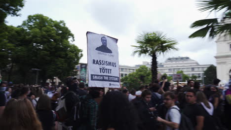 A-following-shot-of-a-woman-holding-a-sign-while-walking-through-a-crowd-and-protesting-against-racism