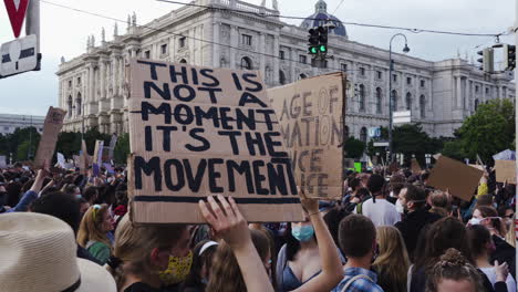 Eine-Aufnahme-Einer-Frau,-Die-Eine-Maske-Trägt-Und-Ein-Schild-Mit-Der-Aufschrift-„Es-Ist-Kein-Moment,-Es-Ist-Die-Bewegung“-In-Der-Hand-Hält,-Während-Sie-Gegen-Rassismus-Protestiert