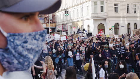 Eine-Aufnahme-Eines-Mannes,-Der-Zum-Schutz-Eine-Maske-Trägt-Und-Eine-Vorbeigehende-Menschenmenge-Beobachtet,-Die-Gegen-Rassismus-Protestiert
