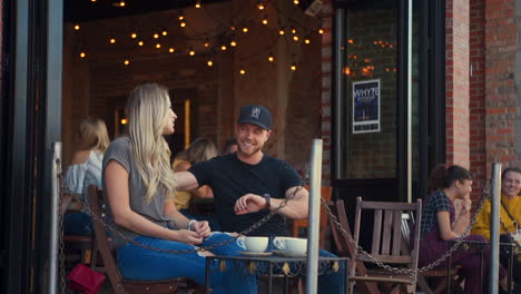 Wide-Two-Shot-of-Couple,-Man-Checks-His-Watch-While-Talking-to-Young-Blonde-Woman-at-Outdoor-Café-Patio