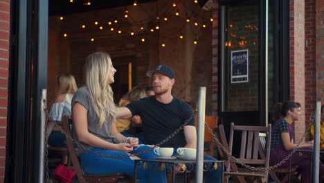 Wide-Two-Shot-of-Couple,-Man-Checks-His-Watch-While-Talking-to-Young-Blonde-Woman-at-Outdoor-Café-Patio