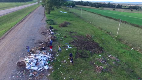 Children-collect-garbage-from-a-roadside-landfill,-drone-shot