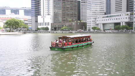 Un-Barco-Que-Transportaba-Turistas-Navegando-Por-El-Río-Singapur-En-Una-Tarde-Soleada,-Rifas-Colocan-Edificios-De-Oficinas