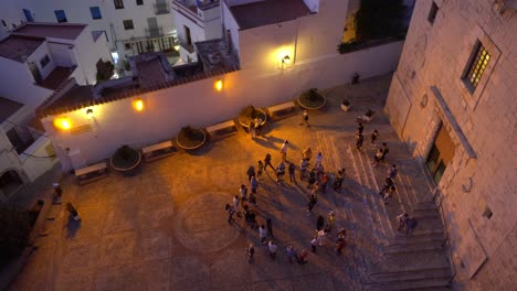 Group-of-people-waiting-in-front-of-a-church-at-dusk-whiile-tourists-walk-in-and-out-shot-from-the-top-with-a-wide-view