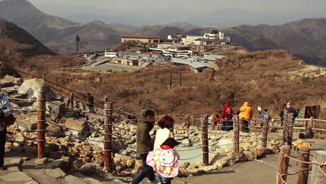Tourists-walking-volcanic-sulphur-attraction-downhill-along-rope-barrier-walkway,-Japan