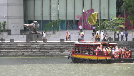 A-boat-ferrying-tourist-at-the-Singapore-river-on-a-sunny-afternoon,-passing-the-offices-in-Raffles-Place-Central-Business-District