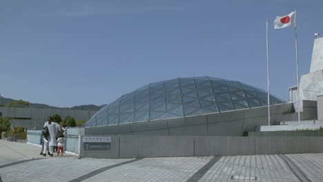 Touristen-Bewundern-Ein-Glaskuppelgebäude-Mit-Einer-Japanischen-Flagge-In-Nagasaki,-Japan