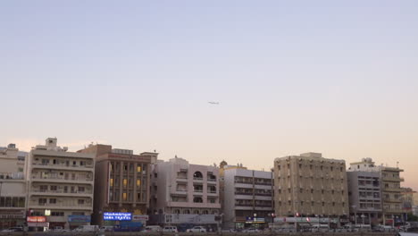 Pájaros-Y-Un-Avión-Volando-Bajo-El-Cielo-Brillante-En-Deira,-Dubai,-Eau-En-Una-Puesta-De-Sol-Con-Edificios-Comerciales-En-El-Fondo---Toma-Amplia