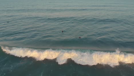 Surfers-learning-to-cruise-on-mild-slow-waves,-on-the-beach-of-Santinho-at-golden-hour