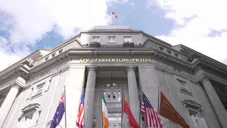 Panning-shot-of-The-Fullerton-Hotel-Singapore-at-the-main-hotel-lobby-with-flags-blowing-in-the-afternoon-sea-breeze-and-the-Singapore-flag-at-the-top-of-the-building