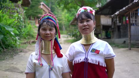 Dos-Mujeres-Kayan-Mirando-Y-Sonriendo-A-La-Cámara-De-La-Tribu-Kayan-Hill-En-La-Aldea-De-Baan-Tong-Luang,-Chiang-Mai,-Tailandia