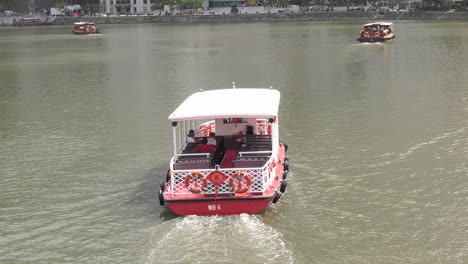 A-boat-ferrying-tourist-streaming-away-from-a-bridge-on-Singapore-river,-afternoon