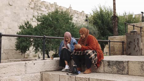 Muslim-women-sitting-together-outside-the-walls-of-an-ancient-city-on-their-smart-cell-phones-technology-developing-countries-culture-ethnic-flare