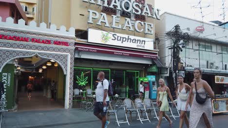 Tourists-walk-past-Khaosan-Palace-Hotel-in-downtown-Bangkok,-Thailand